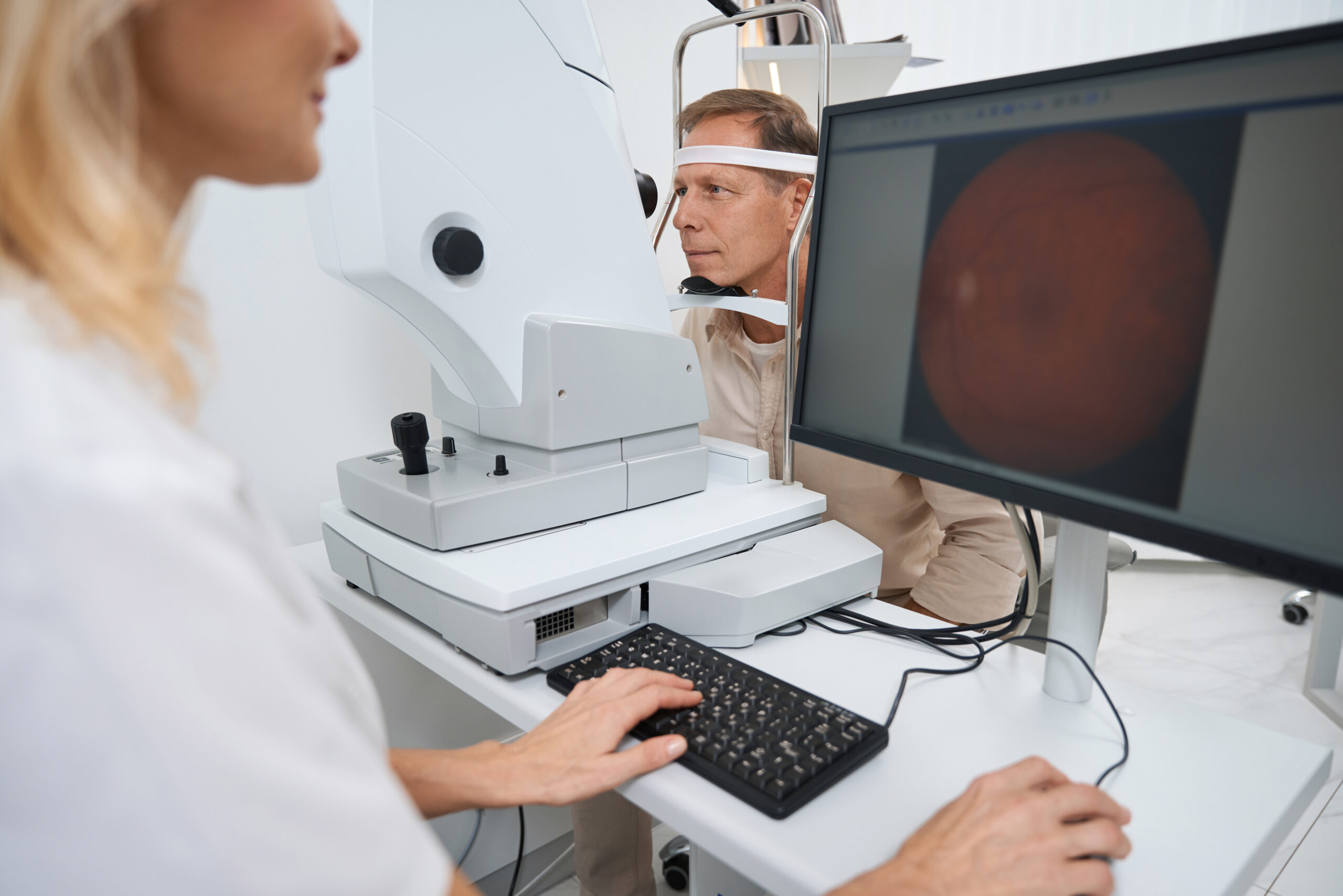 Doctor in white coat sitting at the computer and performing eye examination of eyeball in the hospital