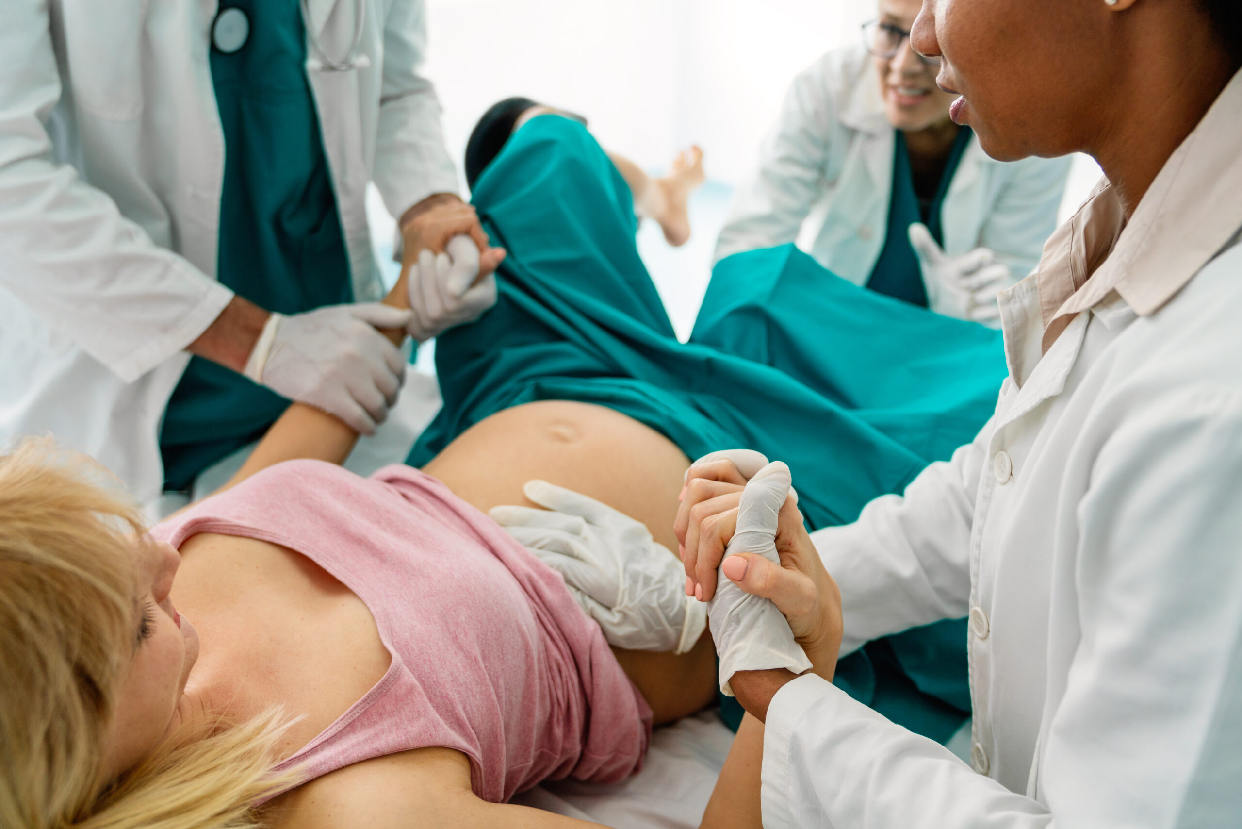 Pregnant young woman pushes to give birth in hospital, obstetrician doctor assisting